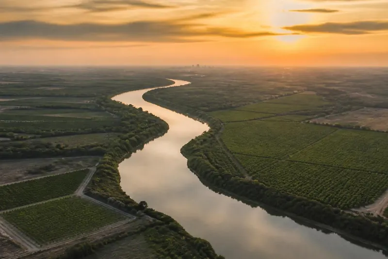 Ilustración: vista aérea del río Bravo entre campos de cultivo al atardecer